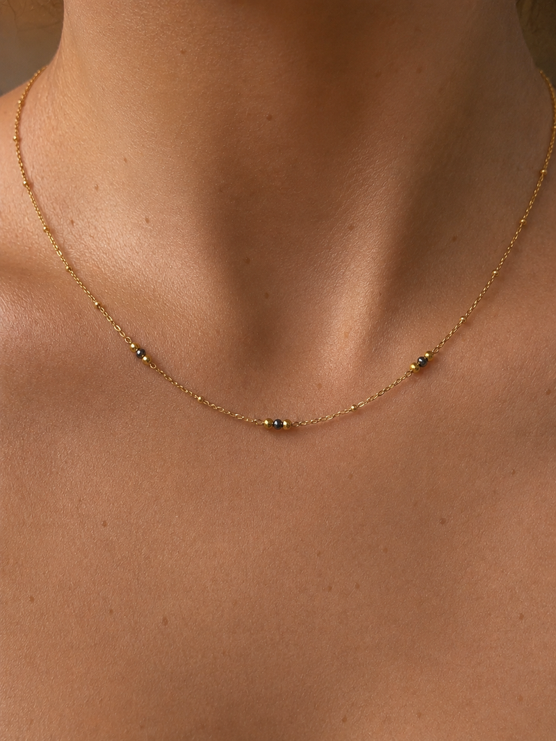 Close-up of a delicate gold necklace with 2 mm grey Keshi freshwater pearls and polished gold bead accents.