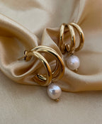 Macro detail of high-luster white pearl charm attached to a polished gold triple-row hoop earring