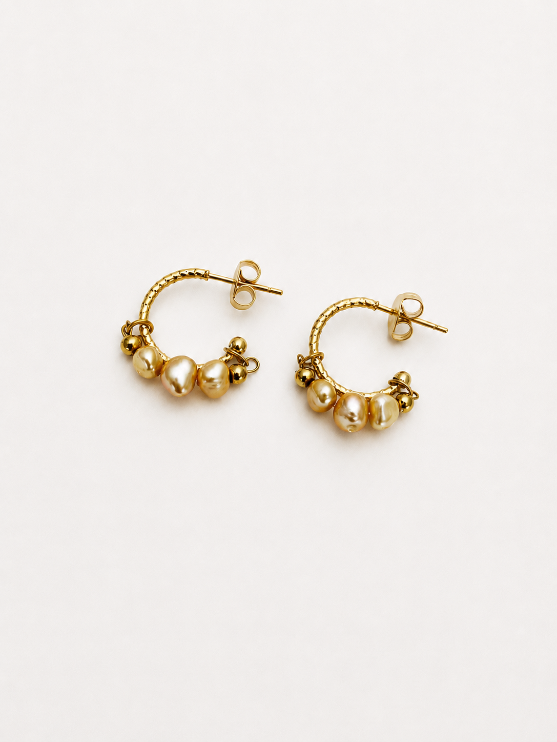 Close-up of 4mm gold cultured freshwater baroque pearls clustered on gold creole hoop earrings