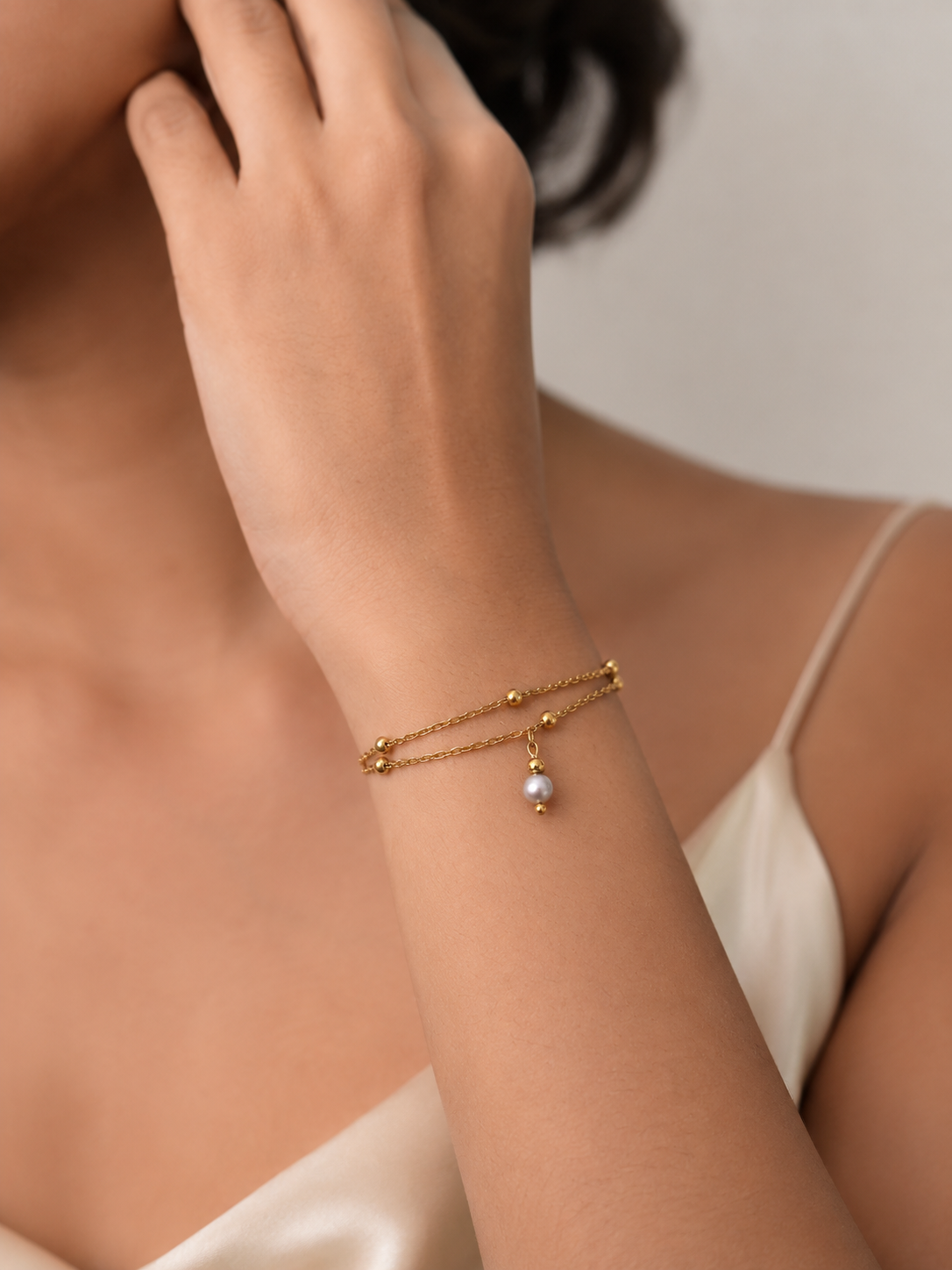 Woman wearing a delicate gold double-chain bracelet with a grey freshwater pearl drop and polished gold beads