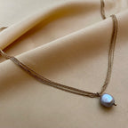 Close-up detail of a grey baroque pearl pendant with metallic luster, suspended on a delicate multi-strand gold chain
