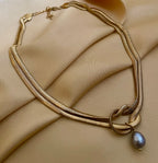 Gold snake chain necklace with a grey baroque pearl pendant. Elegant knotted gold choker styled on a woman for a Parisian chic jewelry look