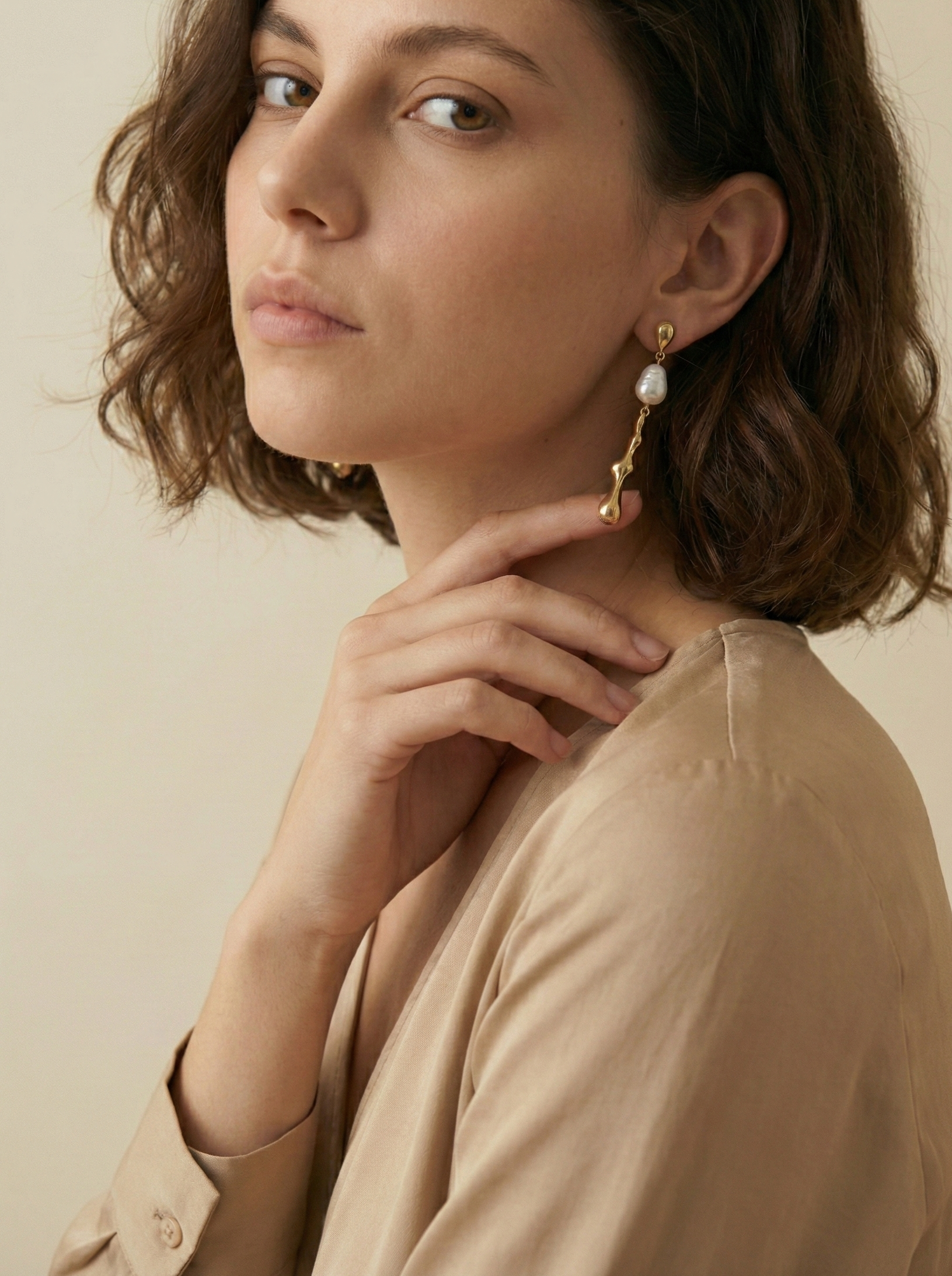 Gros plan sur une boucle d'oreille pendante dorée au design organique avec une perle Keshi blanche lisse et brillant