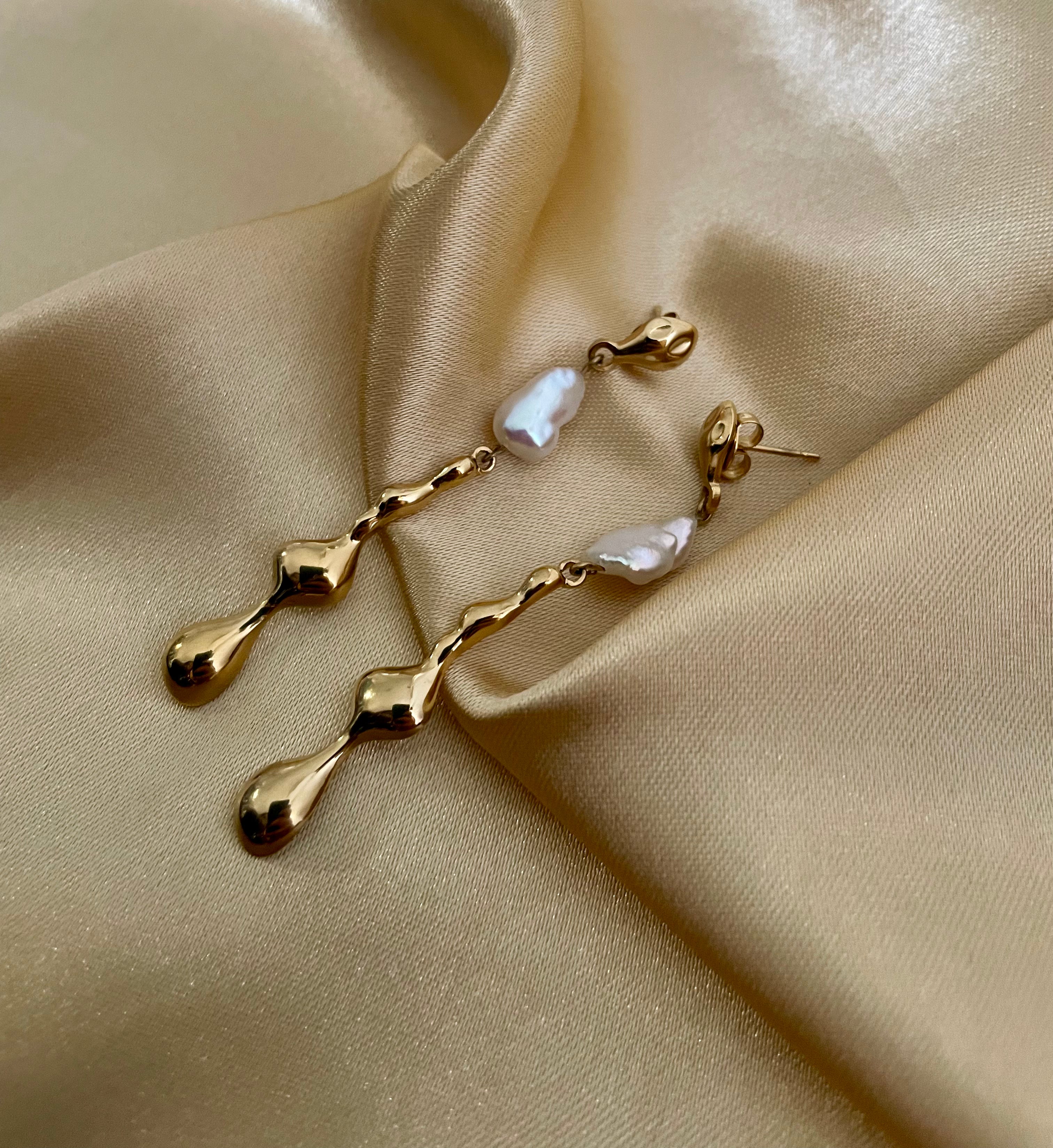 Gros plan sur une boucle d'oreille pendante dorée au design organique avec une perle Keshi blanche lisse et brillante.