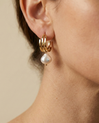 Femme au style parisien chic portant une chemise en soie beige et des boucles d'oreilles en perles naturelles lumineuses