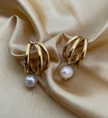 Macro detail of high-luster white pearl charm attached to a polished gold triple-row hoop earring