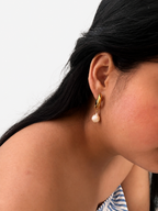 Side view of a chunky gold hoop earring with a 13 mm white baroque freshwater pearl worn on the ear.