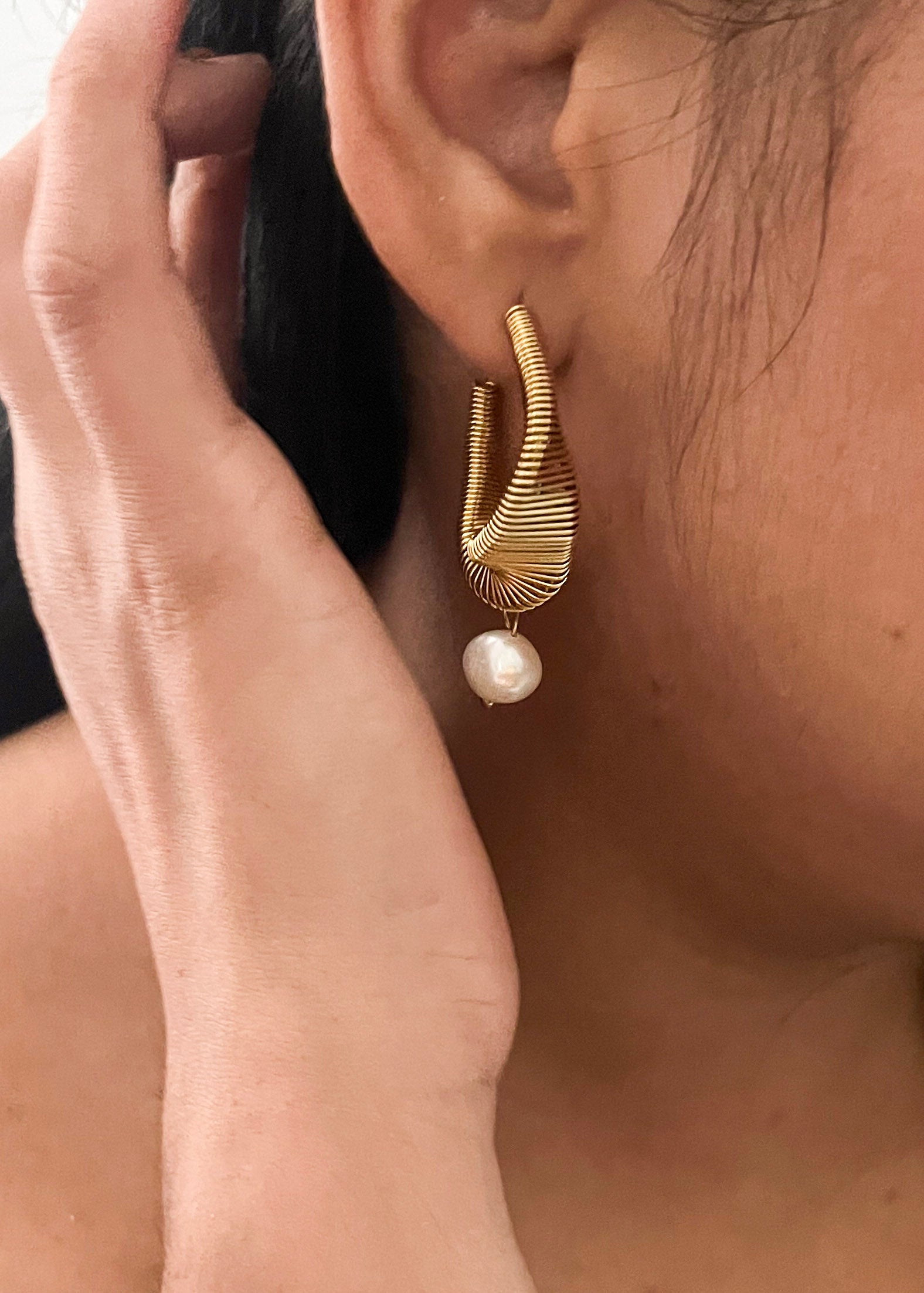 Angled pair of sculptural coiled gold earrings with organic white baroque freshwater pearl drops