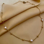 Close-up of a dainty gold chain necklace featuring three small, oval champagne pearls and gold spacer beads