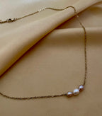 Close-up of a model wearing a dainty gold chain necklace featuring a trio of small pearls: a central white pearl flanked by two pink oval baroque pearls