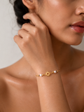 Woman wearing a dainty gold sun charm bracelet with grey baroque freshwater pearls and polished gold beads