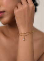 Close portrait of a woman wearing a dainty double-chain bracelet with a small grey freshwater pearl charm
