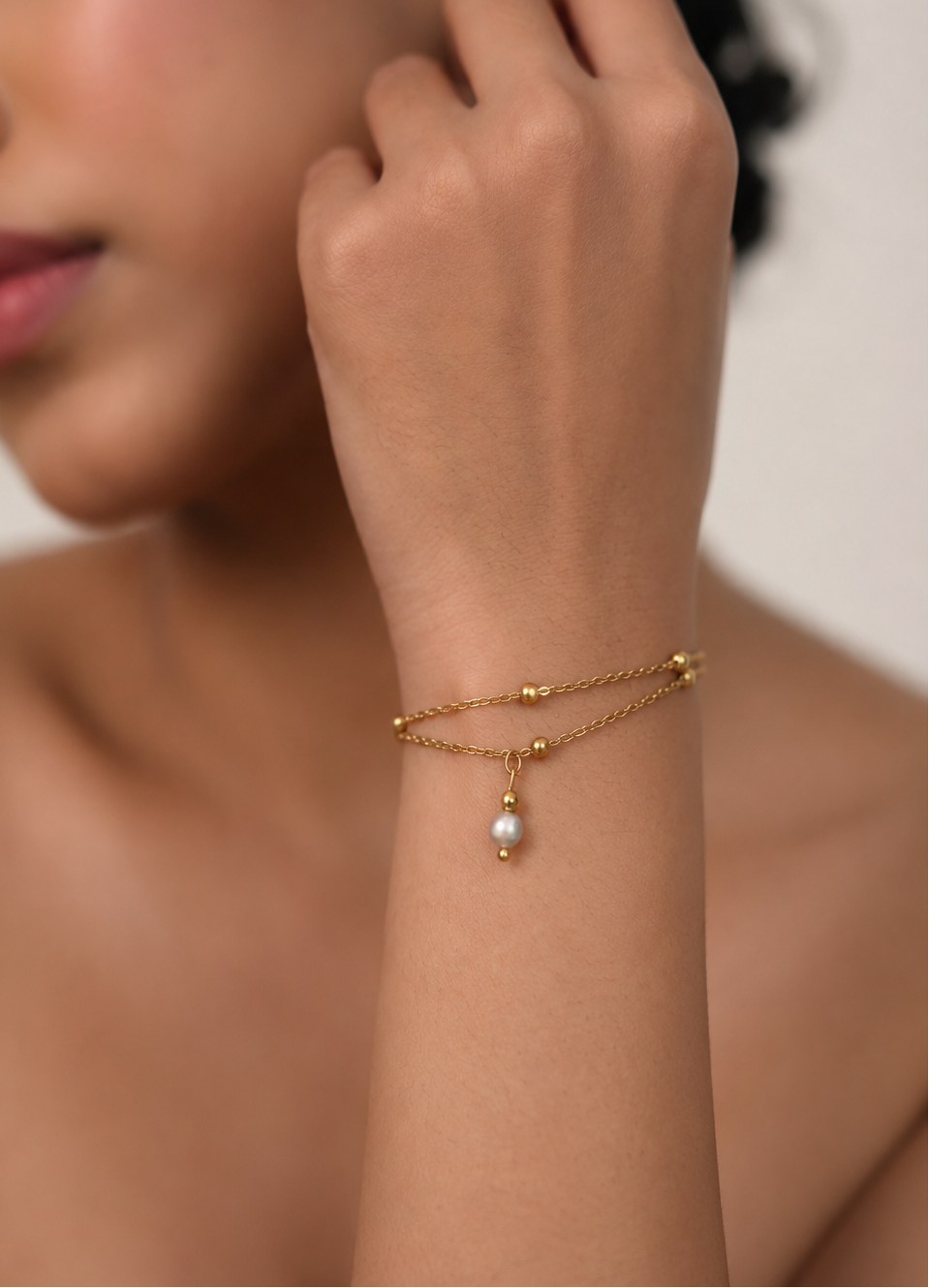 Close portrait of a woman wearing a dainty double-chain bracelet with a small grey freshwater pearl charm