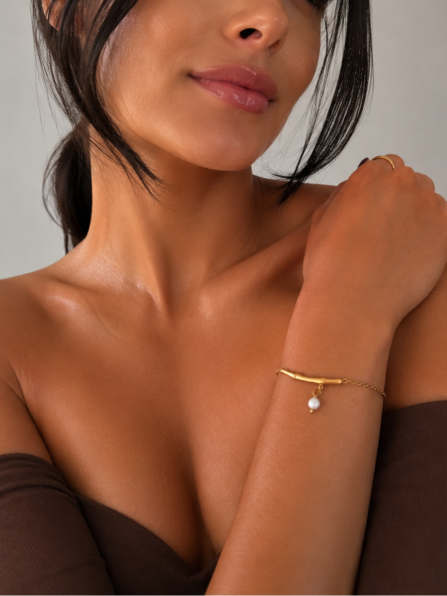 Woman wearing a delicate gold twig bracelet with a grey pearl drop and brown off-shoulder top