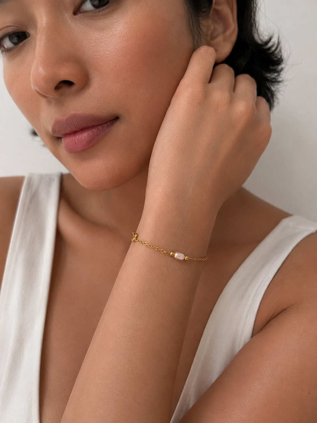 Woman in a white top wearing a dainty pink pearl bracelet with polished gold beads