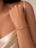 Woman wearing a dainty gold bracelet with small white freshwater pearls and a champagne satin top