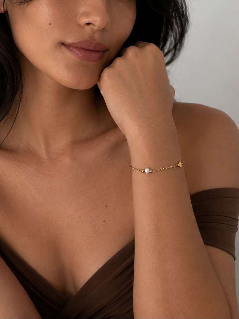 Woman styling a dainty white pearl and gold heart charm bracelet with a brown evening dress