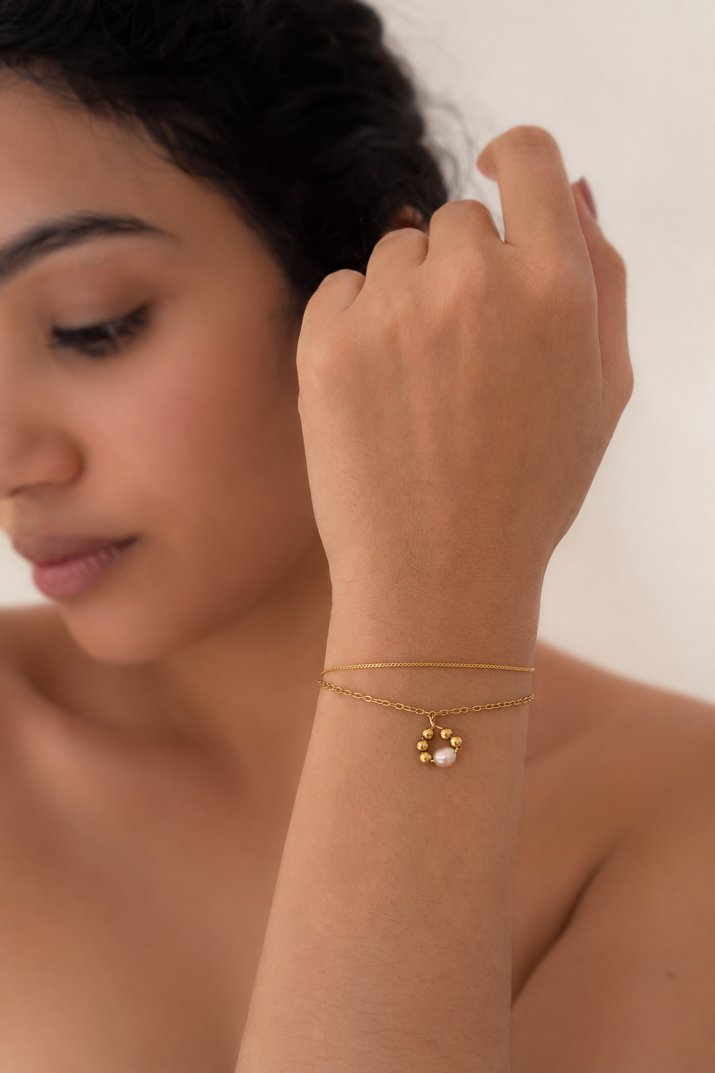 Woman styling a dainty gold double-chain bracelet with a white freshwater pearl pendant