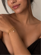 Woman styling a dainty twisted gold bracelet with a white freshwater pearl drop and black evening dress