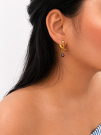 Woman wearing a sculptural gold cross stud earring with a 6 mm dark baroque freshwater pearl drop