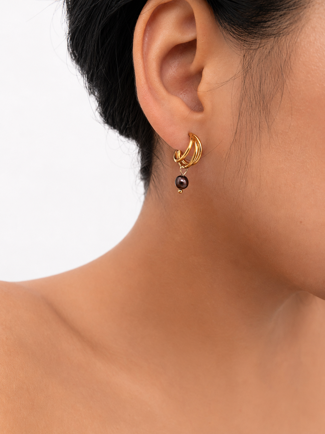 Close-up of a gold triple-hoop earring with a dark baroque freshwater pearl worn on the ear.