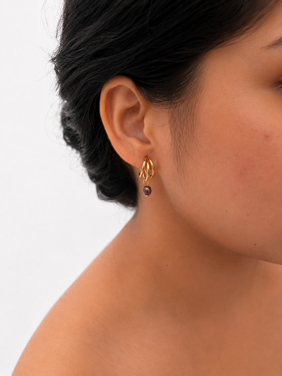 Woman wearing a small gold triple-hoop earring with a 4 mm dark baroque freshwater pearl drop