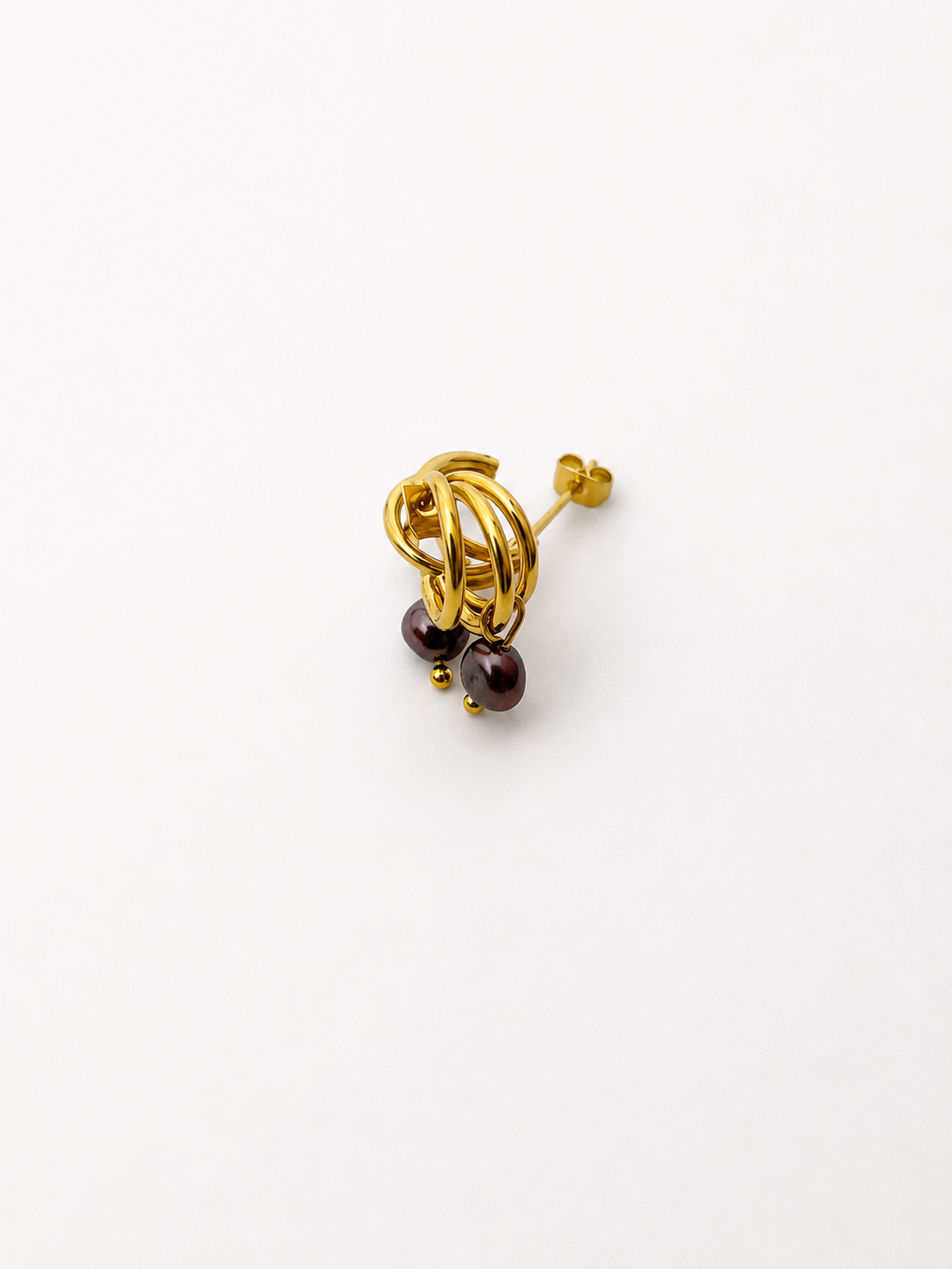 Angled view of small gold triple-hoop earrings with dark baroque freshwater pearl drops.