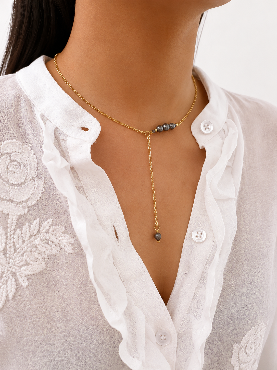 Woman wearing a gold lariat Y-necklace with graduated dark freshwater pearls and a pearl drop pendant.