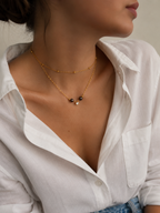 Lifestyle view of a gold layered necklace with dark freshwater pearls, gold beads and a sparkling pendant.