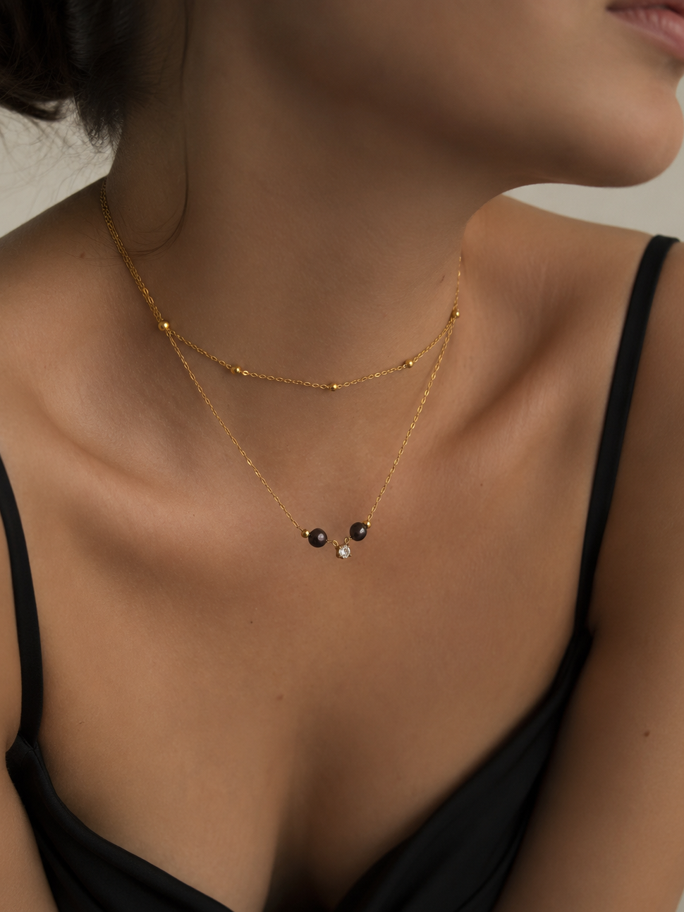 Woman wearing a gold layered necklace with dark freshwater pearls and a sparkling cubic zirconia pendant.