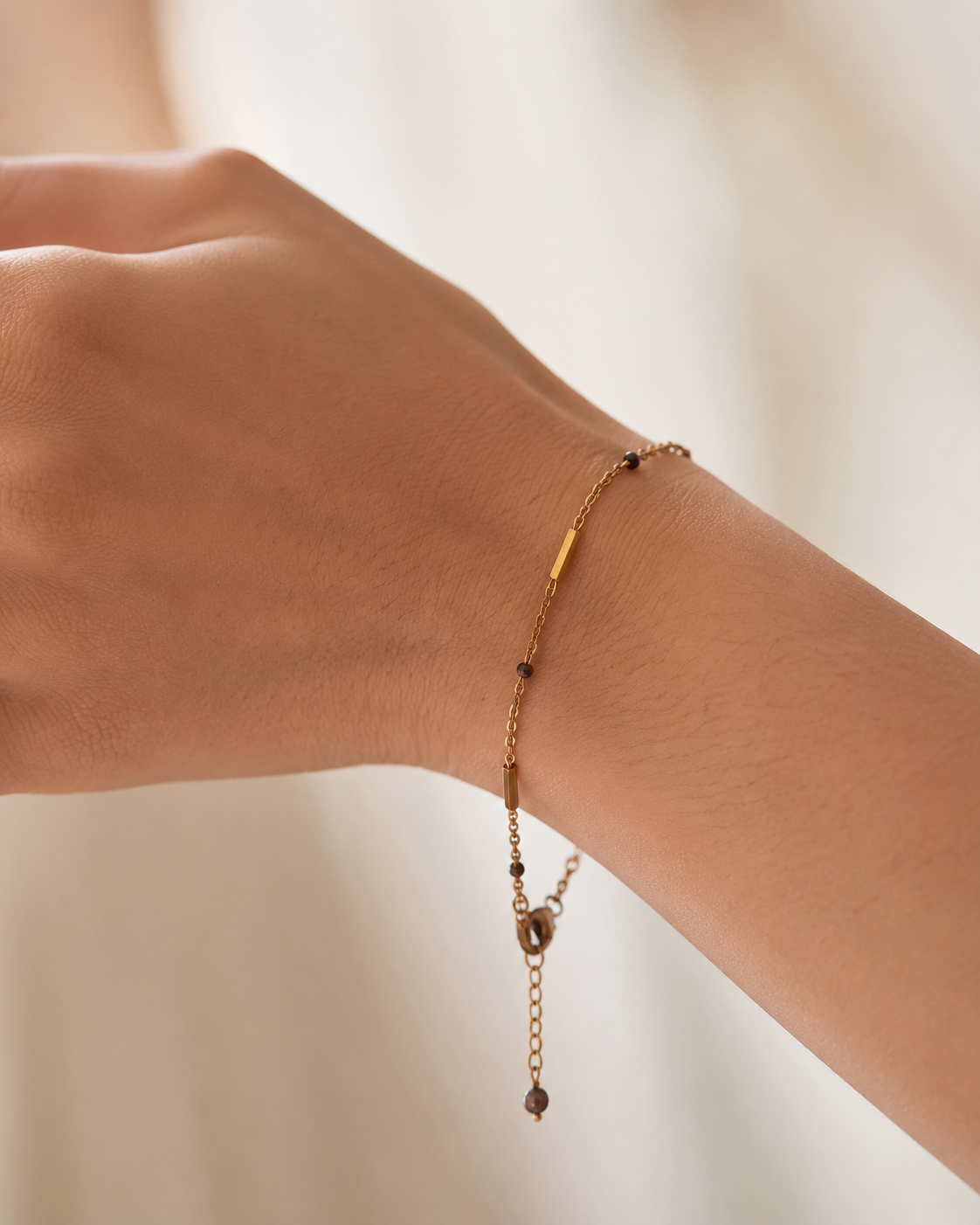 Close-up of a delicate gold bracelet with 2 mm dark grey baroque freshwater pearls worn on the wrist