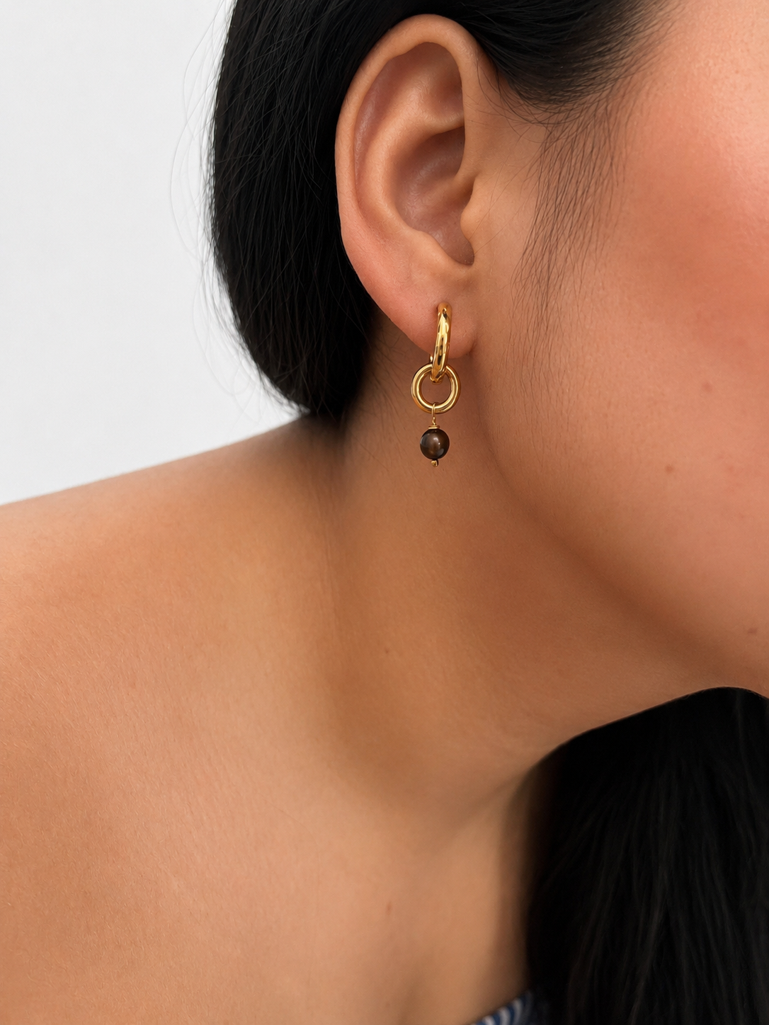 Close-up of a sculptural gold double-hoop earring with a 4 mm dark grey baroque freshwater pearl drop