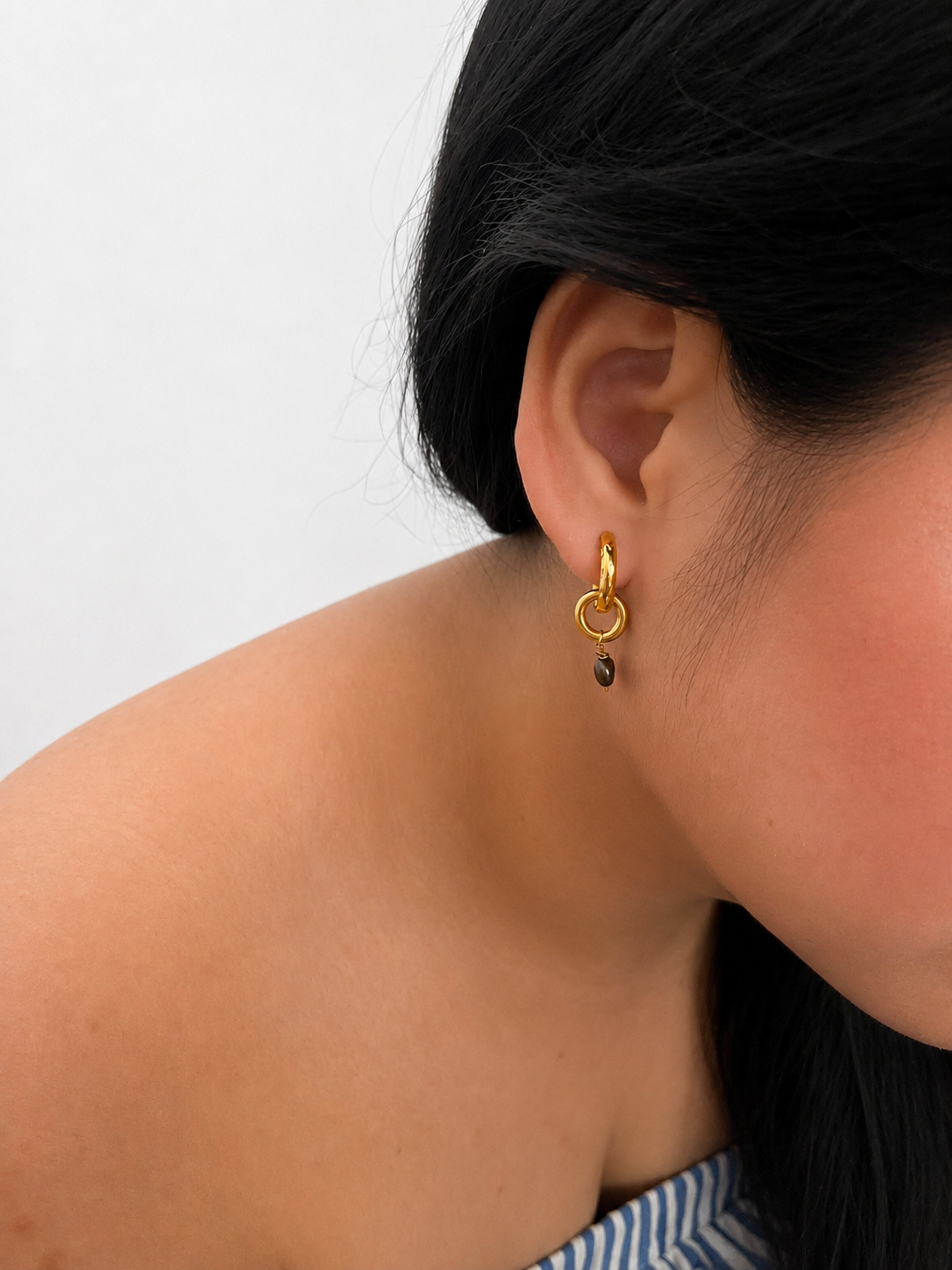 Side view of a gold double-hoop earring with a dark grey baroque freshwater pearl worn on the ear
