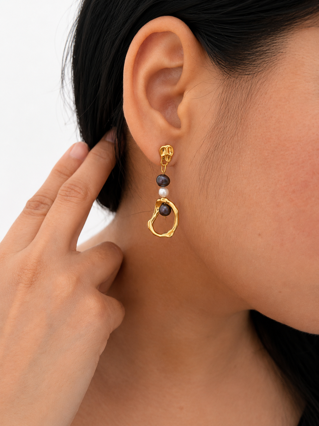 Woman wearing a sculptural gold organic droplet earring with dark grey and grey baroque freshwater pearls