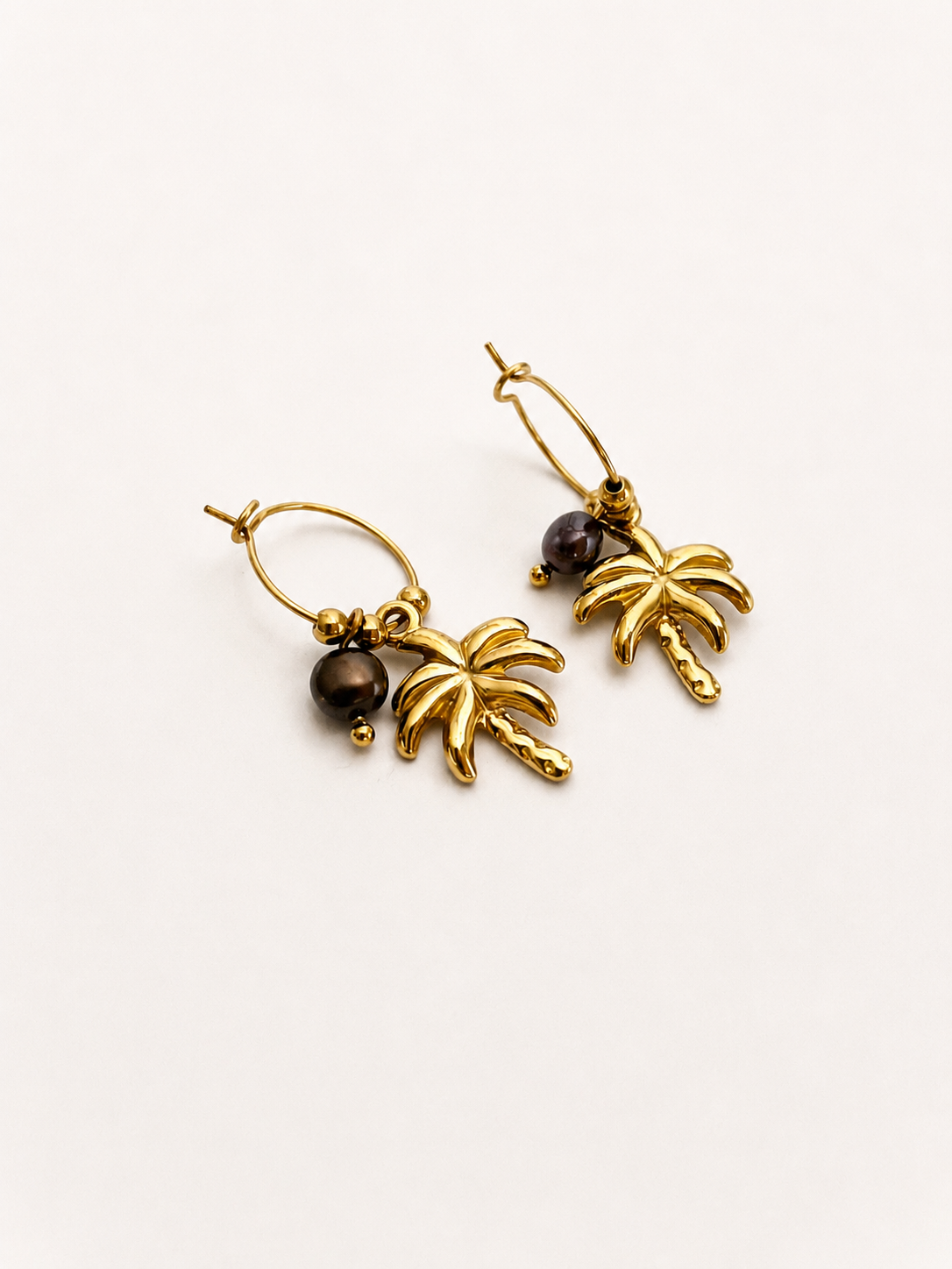 Angled view of gold coconut tree earrings with dark grey freshwater pearl drops.