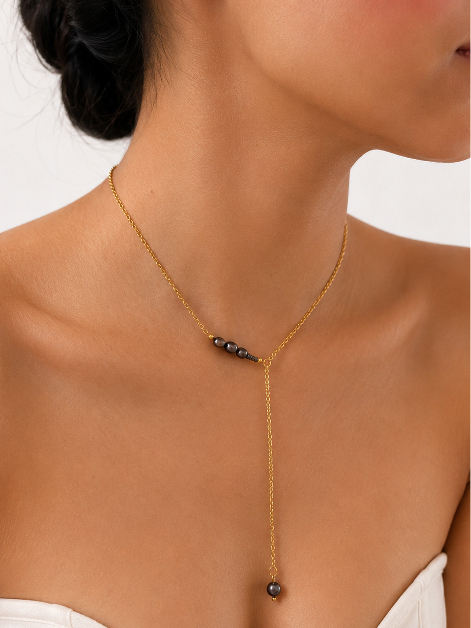 Close-up of a gold Y-necklace with dark round freshwater pearls and a long pearl drop worn on the neck