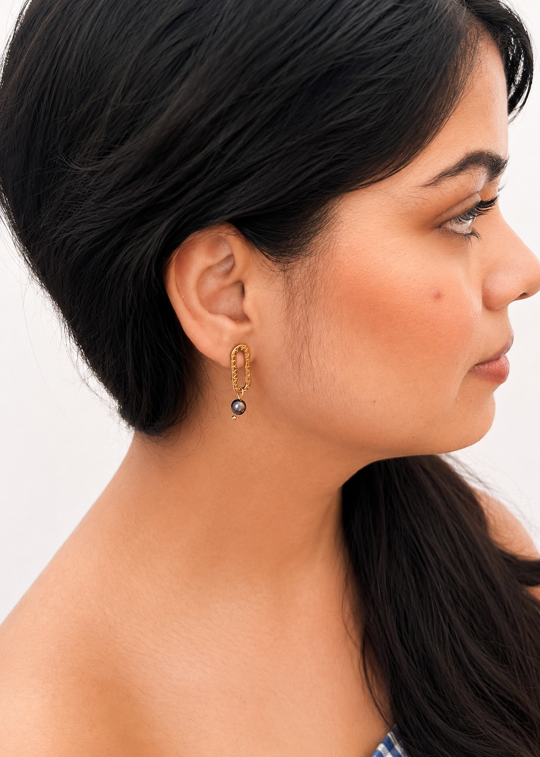 Woman wearing a textured gold stud earring with a dark round freshwater pearl drop