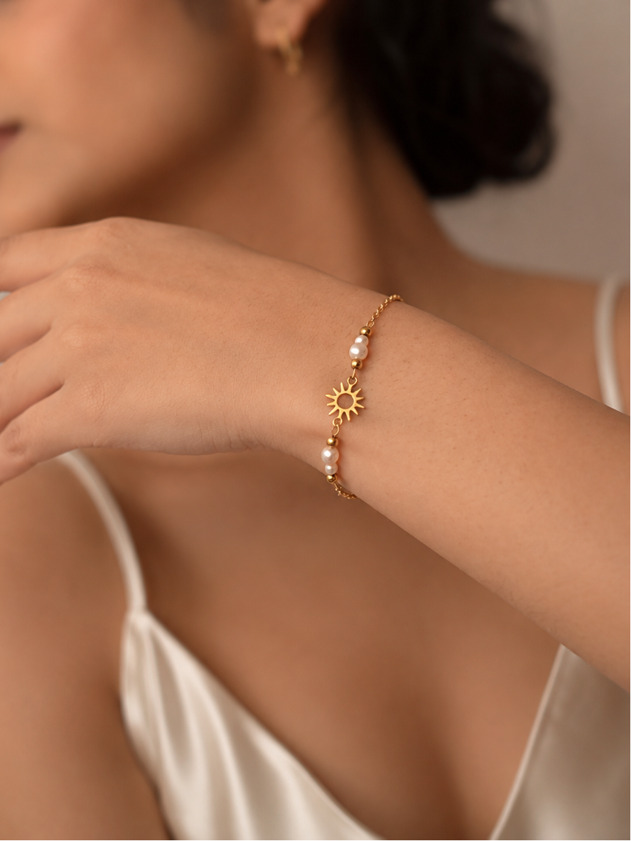 Delicate gold sun charm and white freshwater pearl bracelet styled on the wrist