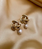 Close-up of gold twisted knot earrings with a white pearl drop