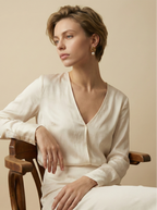 Close-up of gold twisted knot earrings with a white pearl drop, worn by a model in a cream silk blouse