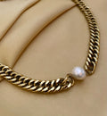 Gold chain necklace with a pearl pendant on a beige fabric background