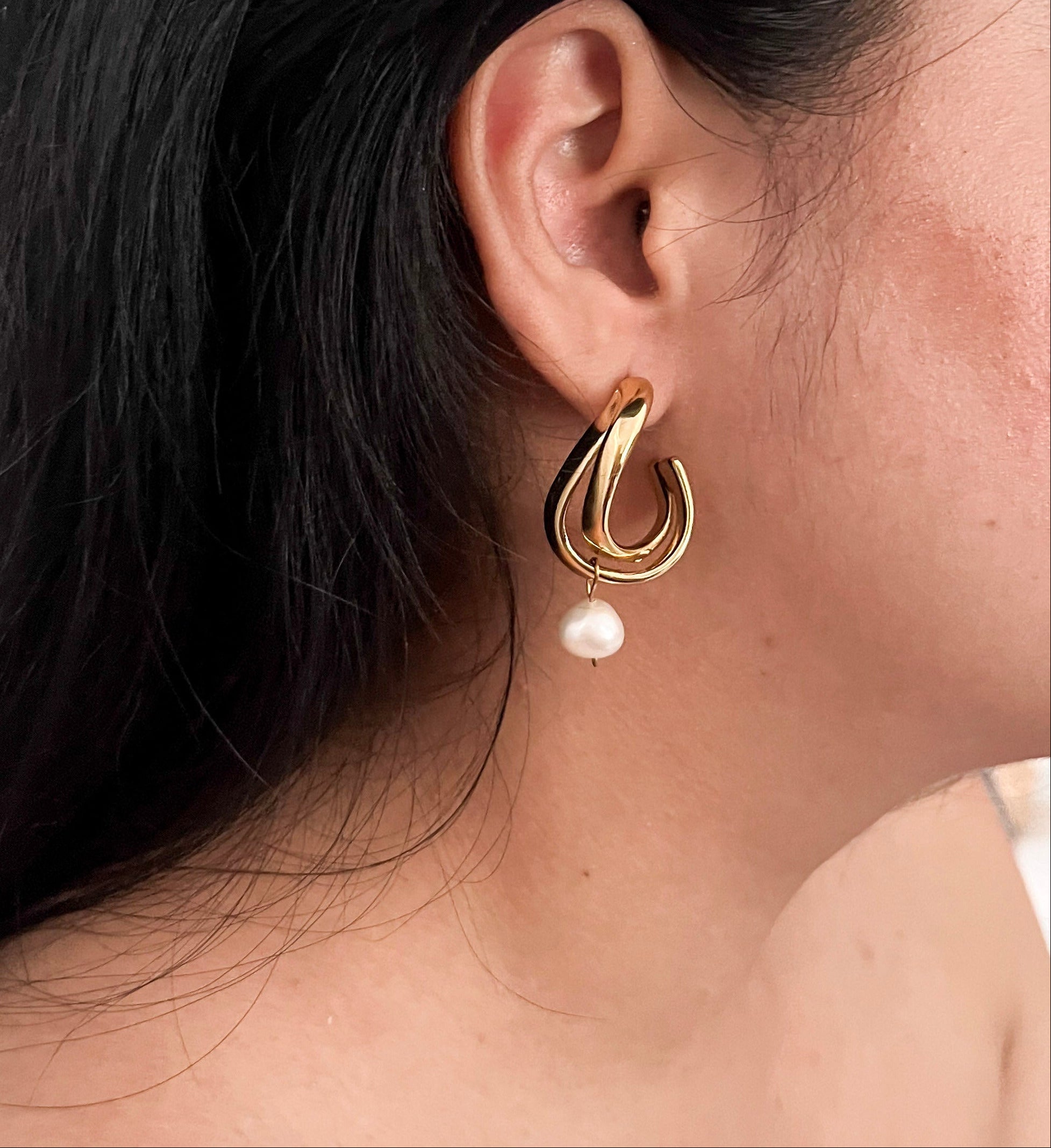 Close-up of intertwined gold hoop earrings with irregular white freshwater pearl drops