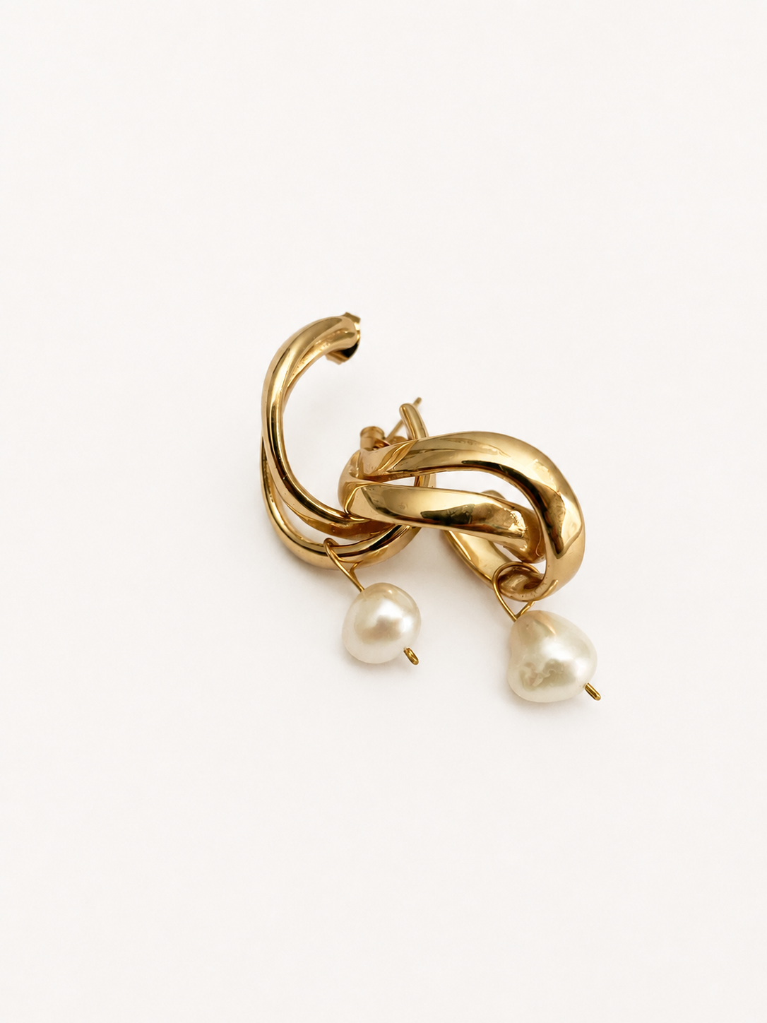 Close-up of intertwined gold hoop earrings with irregular white freshwater pearl drops