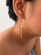 Close-up of a gold drop earring with 4 mm baroque freshwater pearls and a long polished bar pendant.