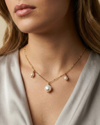 Close-up of a young woman wearing a dainty gold chain necklace featuring a large central baroque white pearl and two smaller accent pearls with gold spacers
