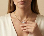 Close-up editorial portrait of a woman wearing a gold oval-link chain necklace featuring a grey baroque keshi pearl and a small white pearl, styled with a deep V-neck ivory silk top