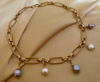 Close-up of a gold link chain necklace featuring dangling white and grey baroque pearl charms on a model wearing an ivory coa
