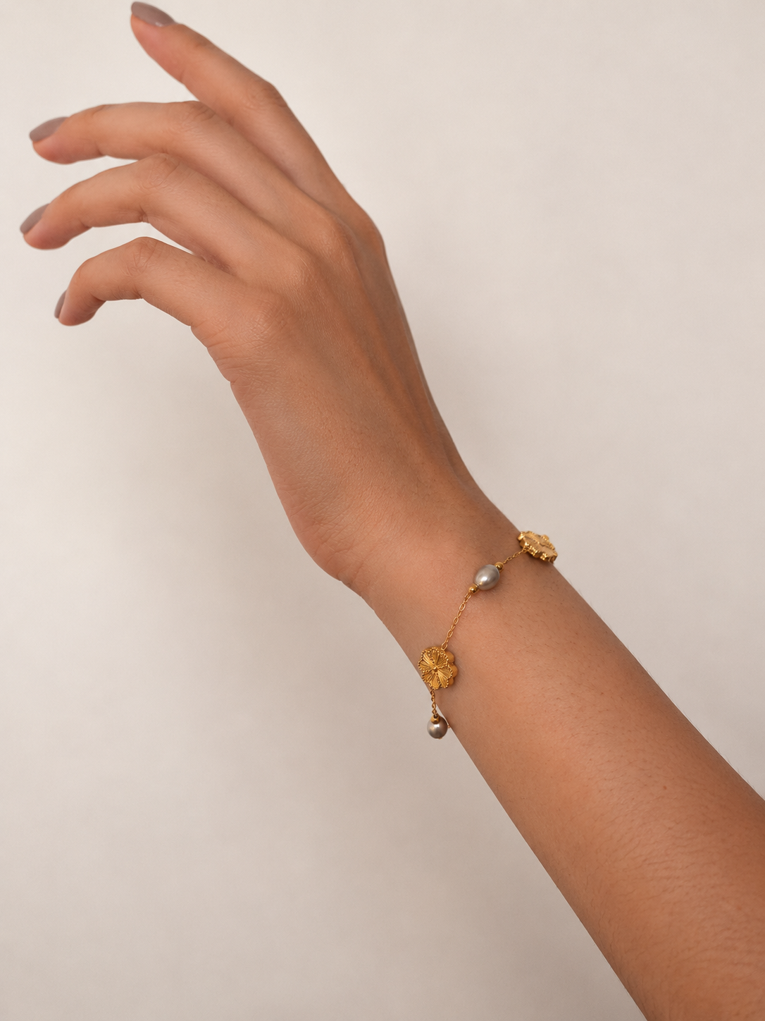 Gold clover bracelet with grey freshwater pearl accents shown on an extended wrist