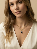Close-up of a model wearing a gold curb chain necklace featuring a round black pearl and small silver pearl pendant, styled with an ivory silk top