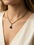 Close-up of a model wearing a gold curb chain necklace featuring a round black pearl and small silver pearl pendant, styled with an ivory silk top